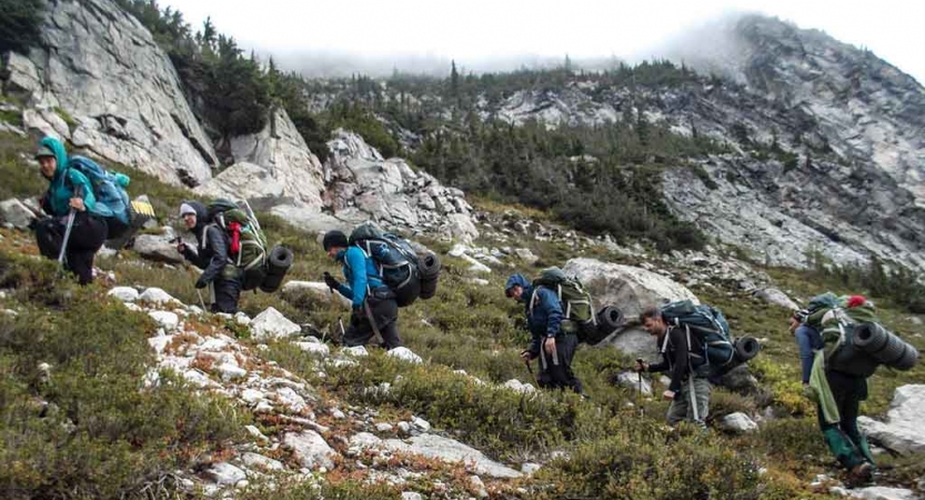 teens backpacking through rocks and greenery on outward bound course